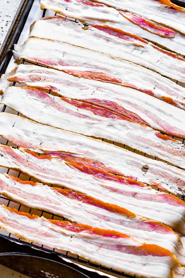 Raw bacon strips on a wire rack, set in a baking tray.