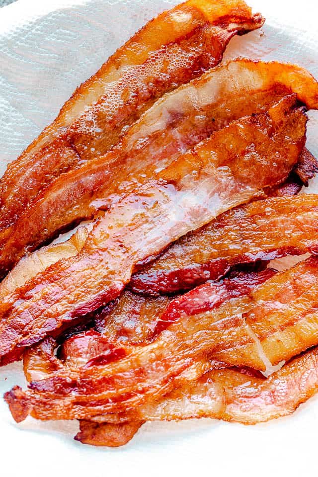 Cooked bacon draining on a paper towel-lined plate.
