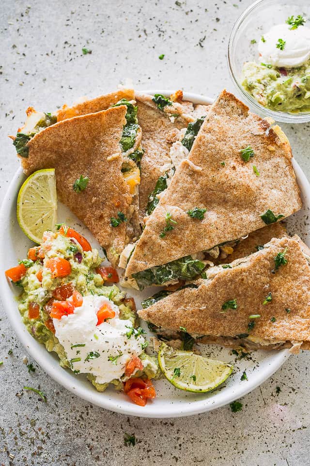 A plate of baked quesadillas with sour cream and quac.