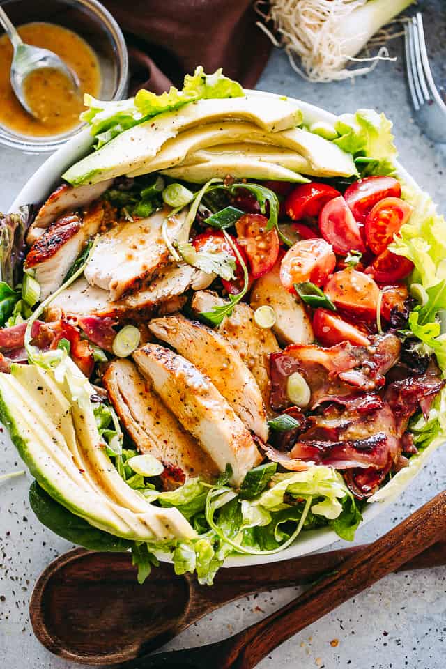 A garden salad with tomatoes, avocado, chicken, bacon, green onions, and more.