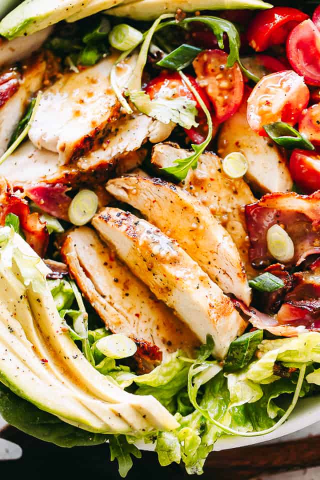 Close-up shot of a salad with sliced chicken breast, avocados, bacon, and more.