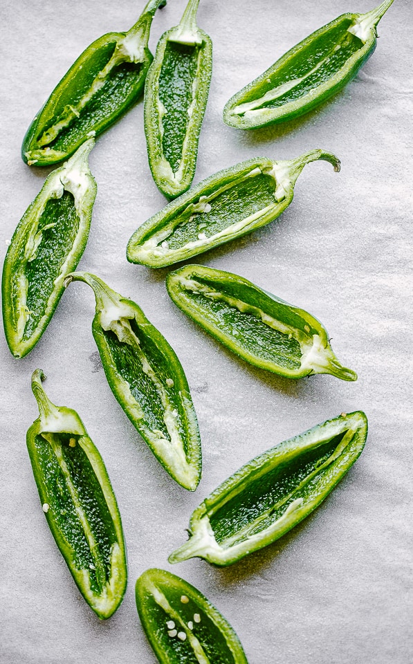 Halved and seeded jalapenos on a parchment-lined surface.