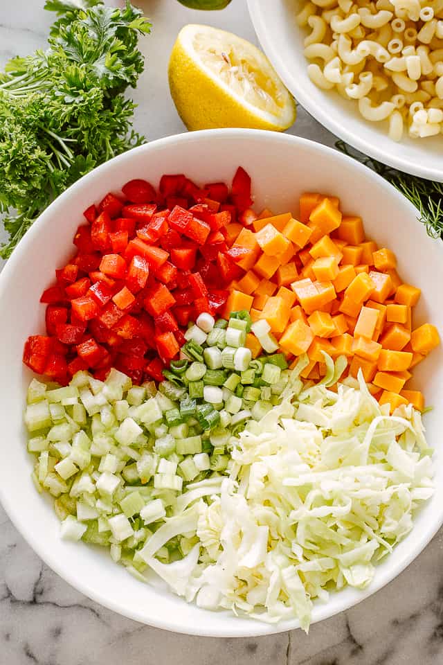 Chopped red bell pepper, diced cheddar, shredded cabbage, diced celery, and sliced green onions in a large bowl.
