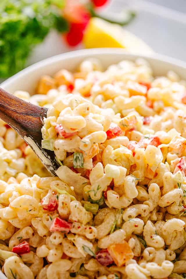 Creamy pasta salad with veggies, being stirred with a wooden spoon.