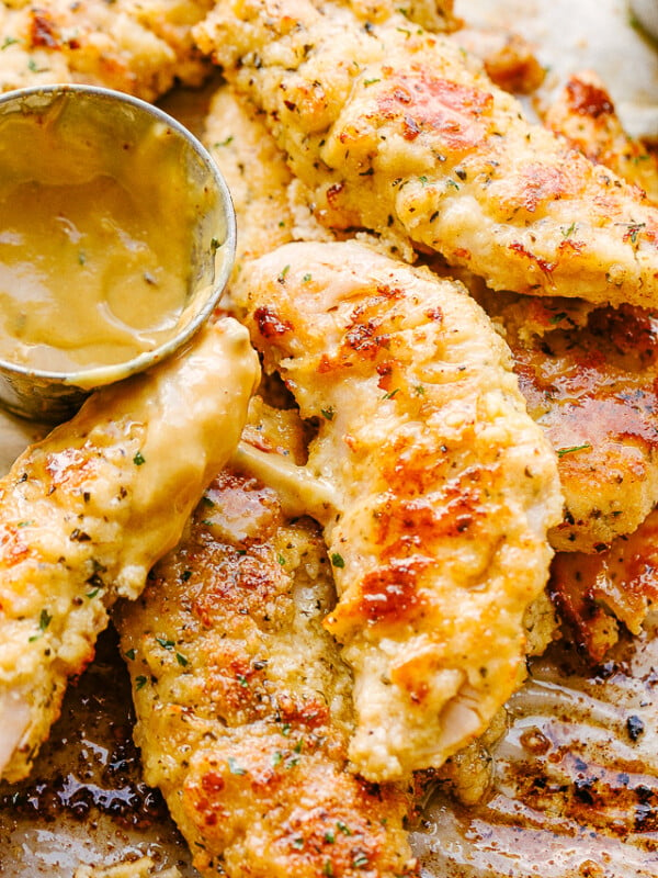 A close-up photo of chicken tenders and a small serving bowl filled with mustard sauce.