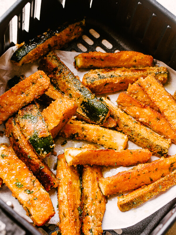 Fried zucchini in the basket of an air fryer.