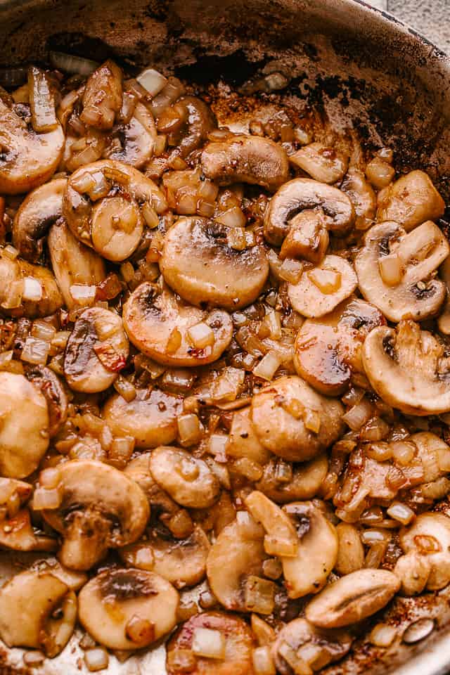 Mushrooms and onions cooking in a skillet.