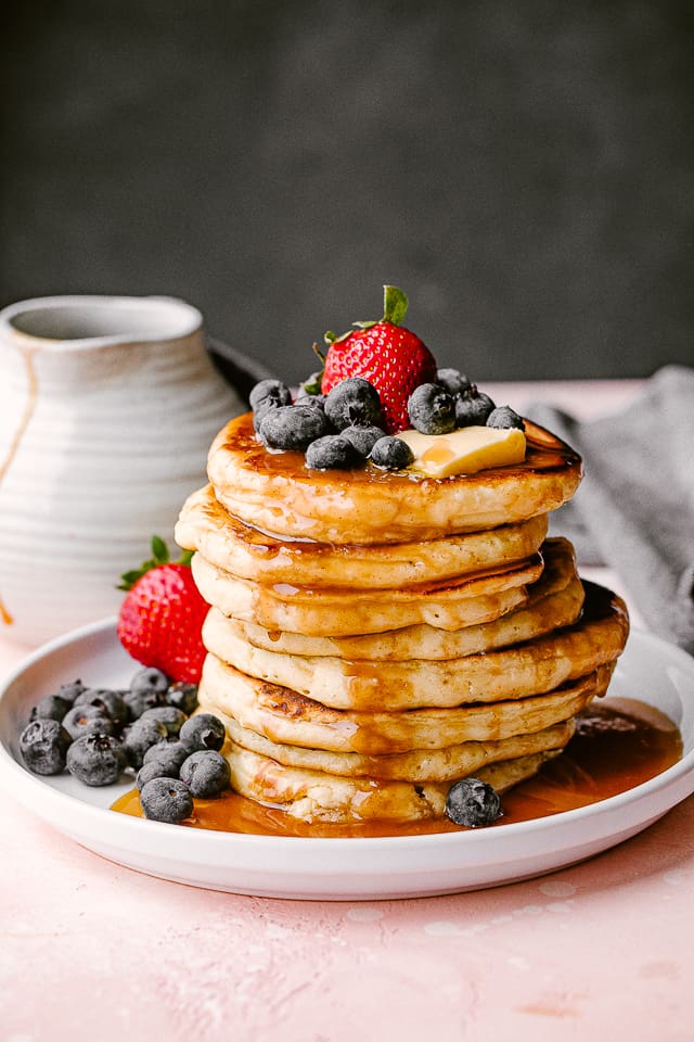Stack of fluffy homemade pancakes, topped with berries, syrup, and butter.