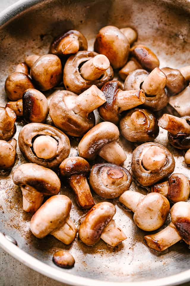 Placing button mushrooms in a skillet to cook.