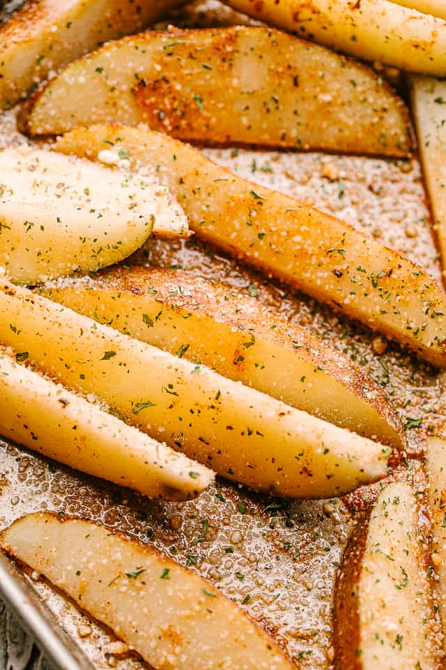 Close-up shot of seasoned, baked potato wedges on a baking sheet.