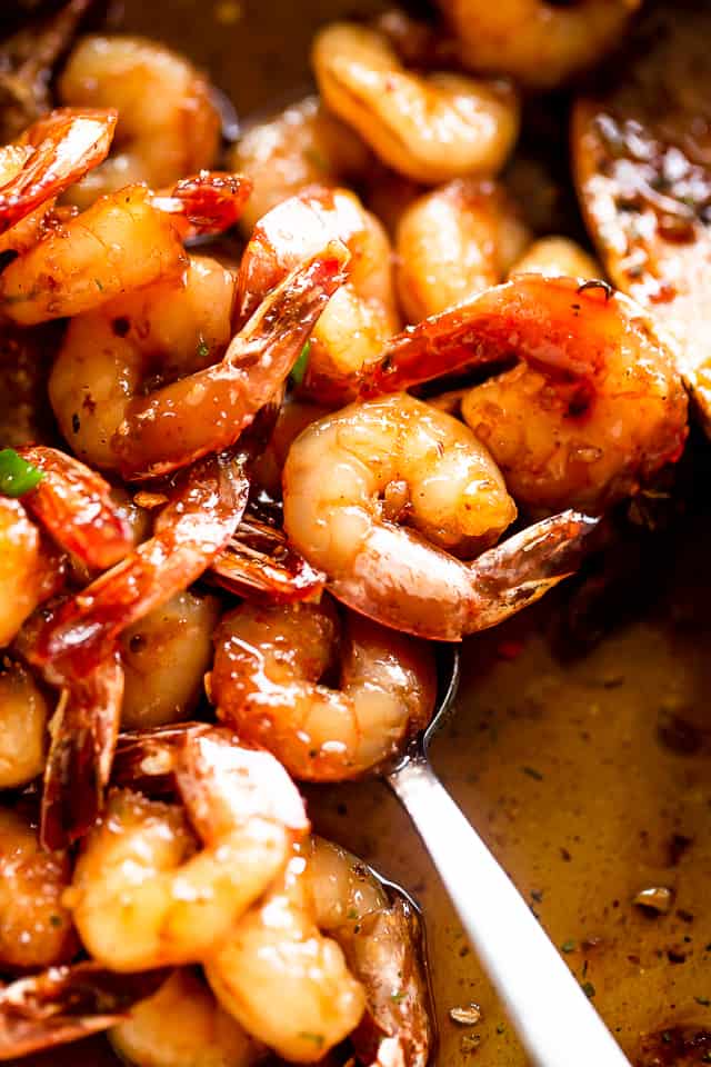 Close up of honey garlic shrimp, tails on, with a spoon lifting some of the shrimp.