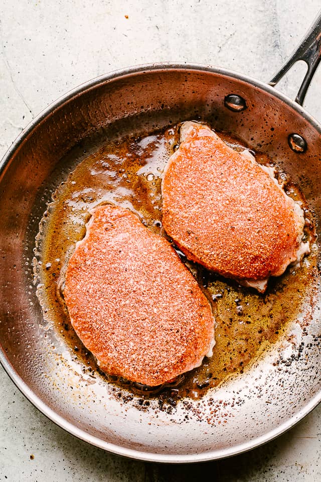 Frying smothered pork chops in a skillet.