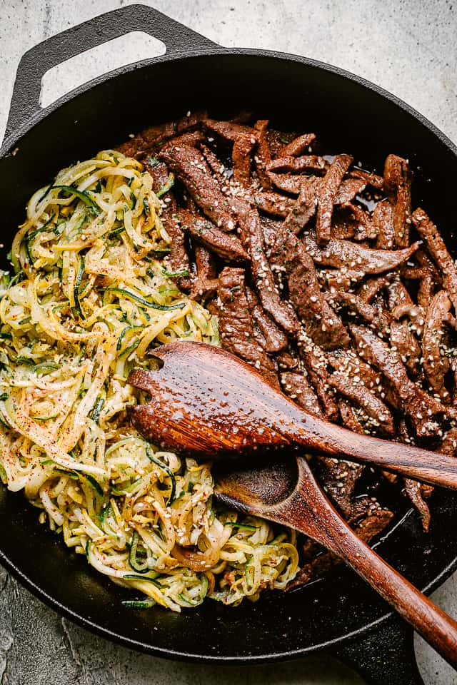 Sliced steak and zucchini noodles in a cast-iron skillet.