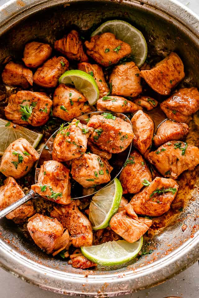 Seasoned chicken pieces in a skillet, garnished with herbs and citrus.