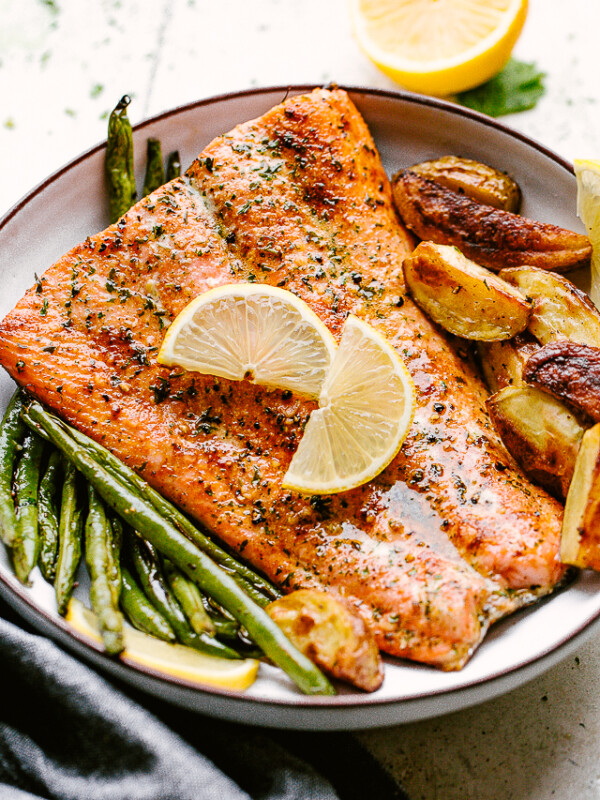 Broiled salmon plated with potatoes and greenbeans and garnished with lemon wedges