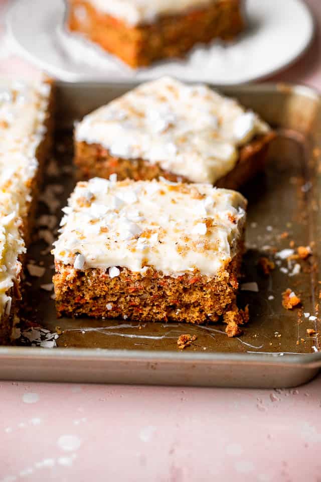 Two slices of carrot cake topped with frosting and coconut, in a baking pan.