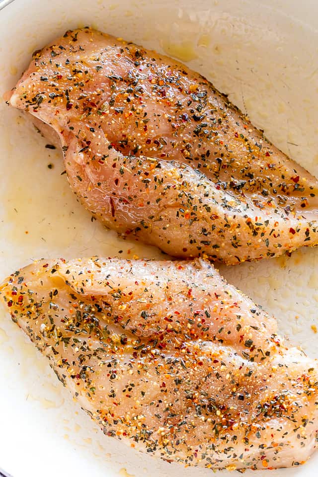 Raw chicken, sprinkled with seasonings and coated in olive oil.