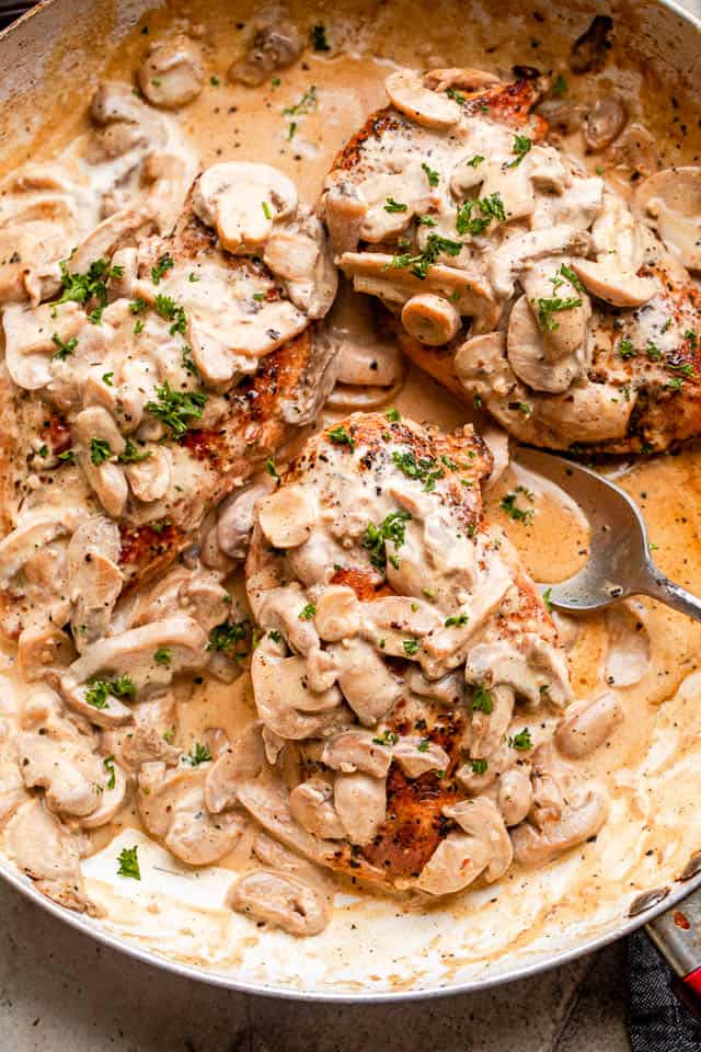 Creamy mushrooms spooned over chicken in a skillet garnished with fresh herbs