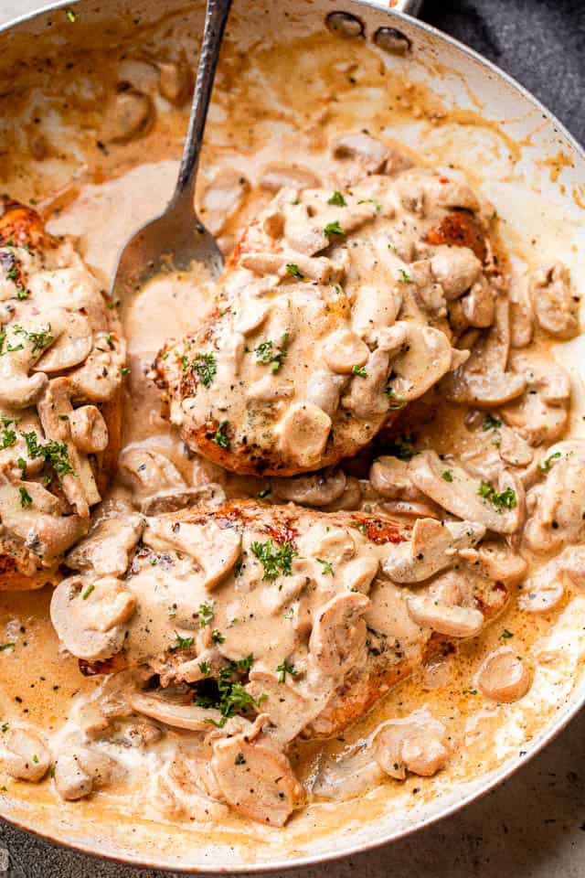 Creamy mushrooms spooned over chicken in a skillet garnished with parsley