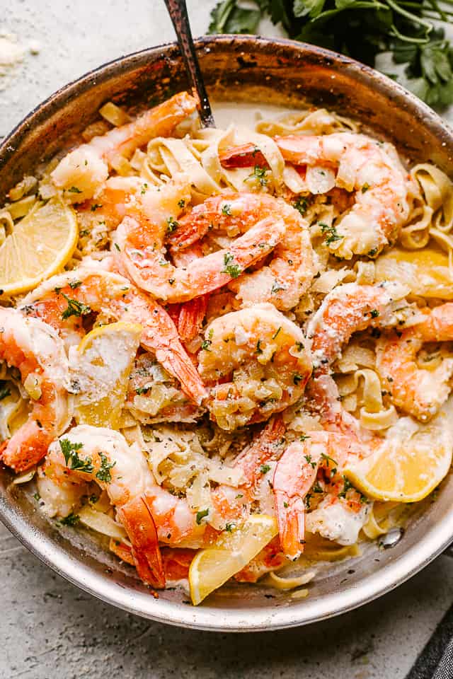 A pot of creamy shrimp and pasta, garnished with lemon slices.