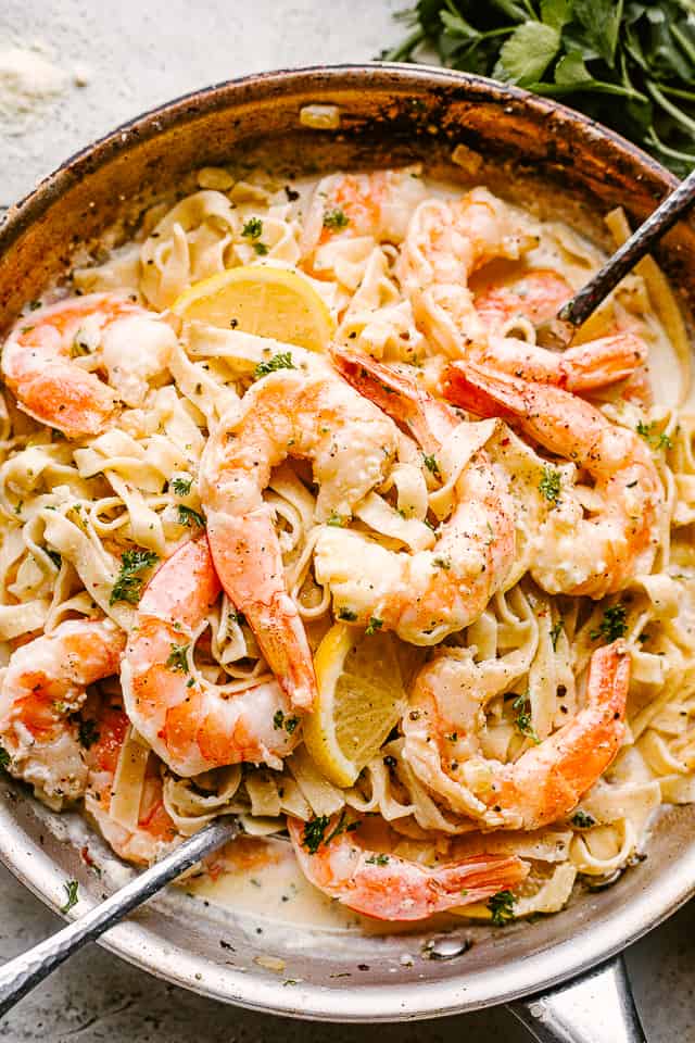 Pasta and shrimp in a creamy sauce, with serving spoons stuck into the pasta.