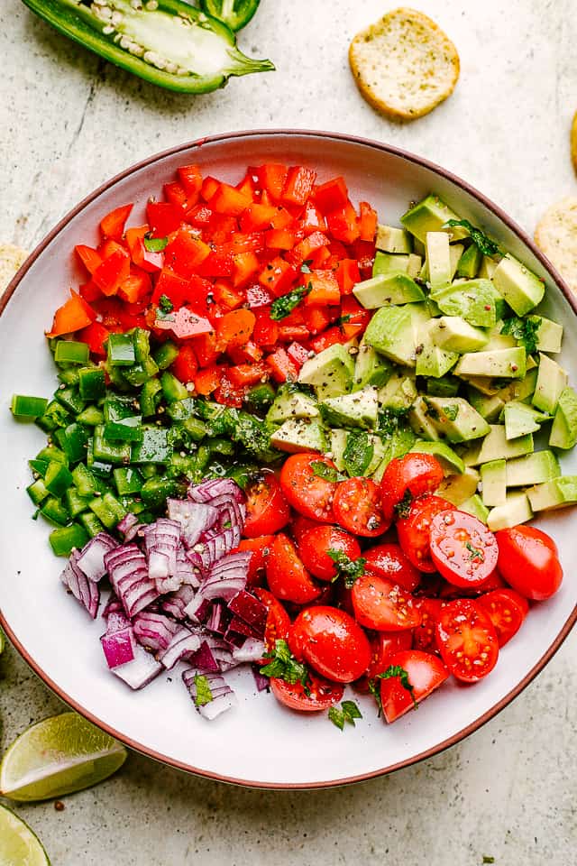 Red bell pepper, diced avocado, halved cherry tomatoes, chopped red onion, and finely diced jalapeno in a bowl. These ingredients have not been stirred yet.