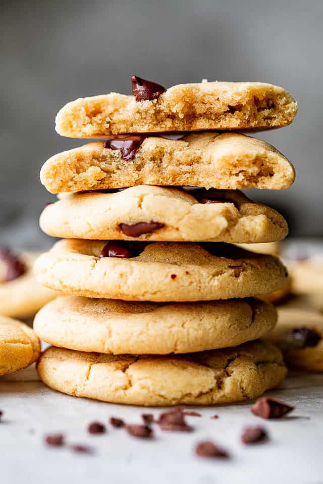 A stack of perfect chewy chocolate chip cookies with one broken in half on top. 