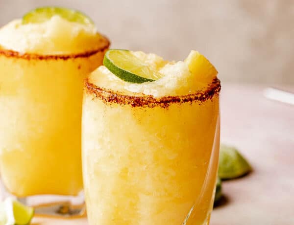 Two glasses of frozen pineapple margaritas with a chili salt rim garnished with lime and mint.