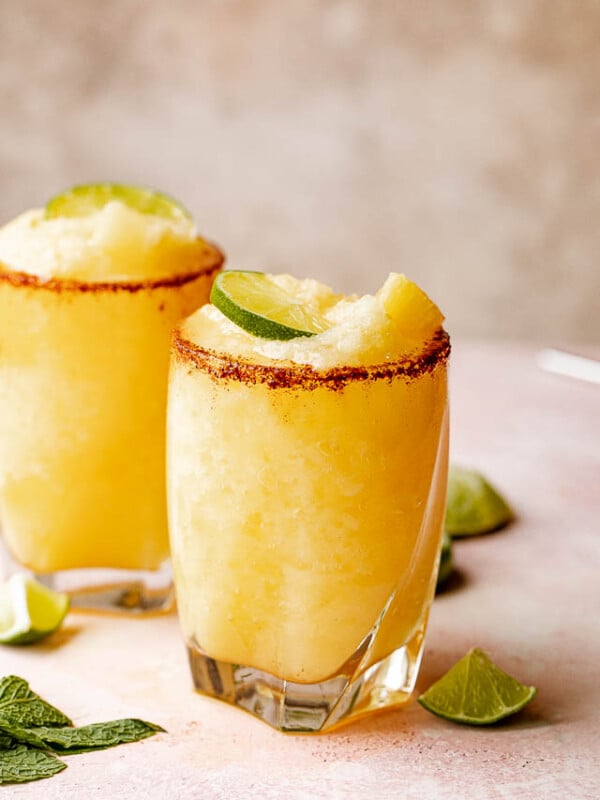 Two glasses of frozen pineapple margaritas with a chili salt rim garnished with lime and mint.