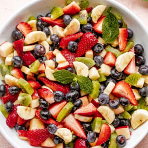 Fresh fruit salad in a large white bowl garnished with fresh mint leaves.