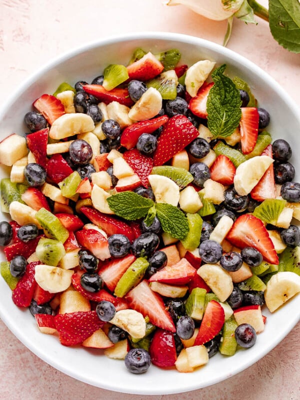 Fresh fruit salad in a large white bowl garnished with fresh mint leaves.