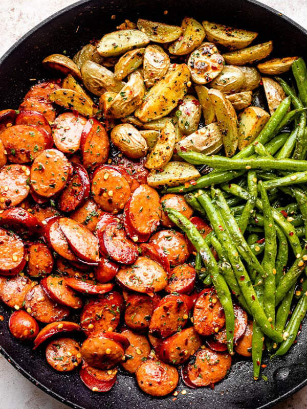 close up of potatoes, green beans, and sausage slices in a black skillet