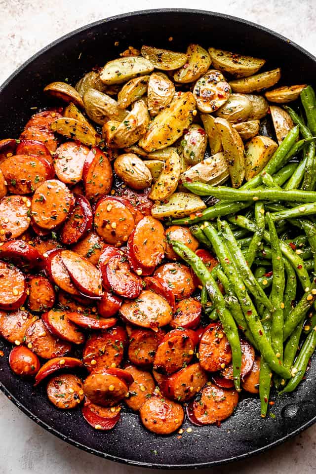 close up of potatoes, green beans, and sausage slices in a black skillet