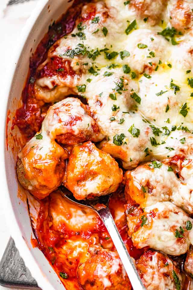 scooping out baked meatballs from a white baking dish