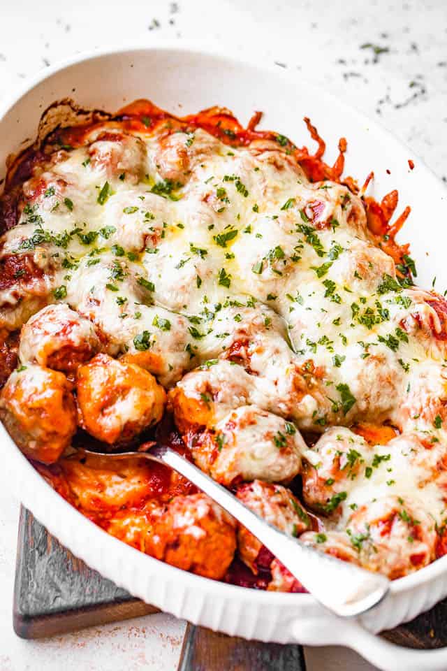white baking dish filled with baked meatballs covered in marinara sauce and melted cheese