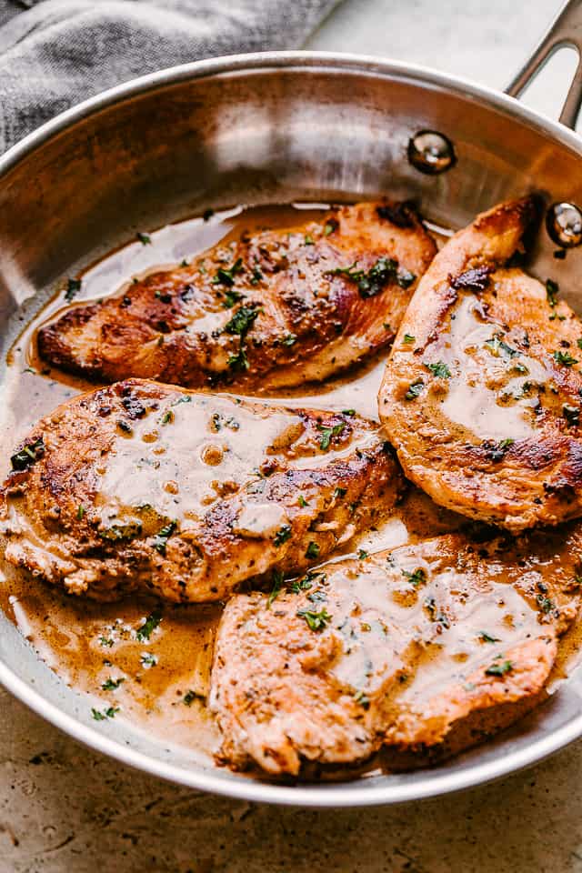 side view of four cooked chicken breasts topped with balsamic sauce and parsley