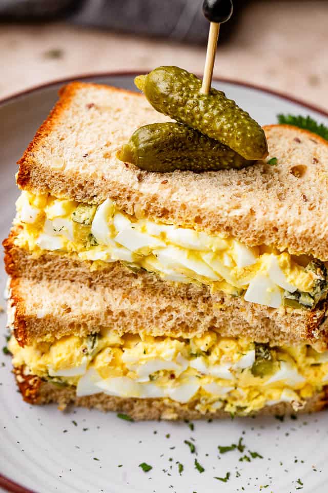 stacked up egg salad sandwich with pickles pinned on top of the sandwich