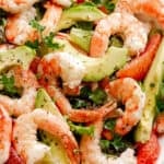 cooked shrimp, avocado slices, and salad greens tossed together in a white serving bowl