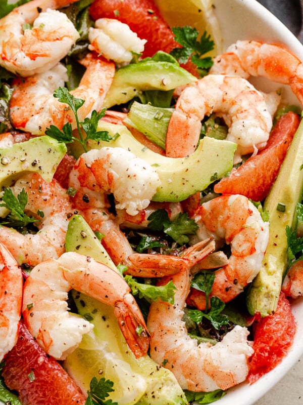 cooked shrimp, avocado slices, and salad greens tossed together in a white serving bowl