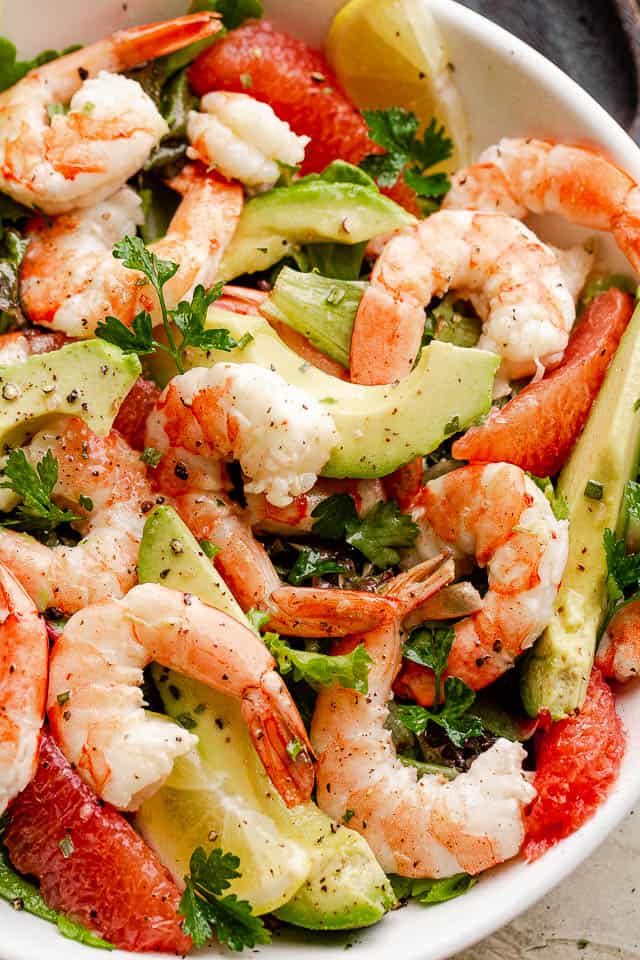 cooked shrimp, avocado slices, and salad greens tossed together in a white serving bowl