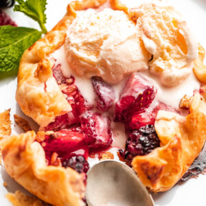 top view of an ice cream topped mini berry galette with a metal spoon and fork set on the side of it.