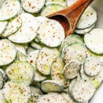 salad bowl filled with sour cream covered cucumbers sprinkled with cracked black pepper