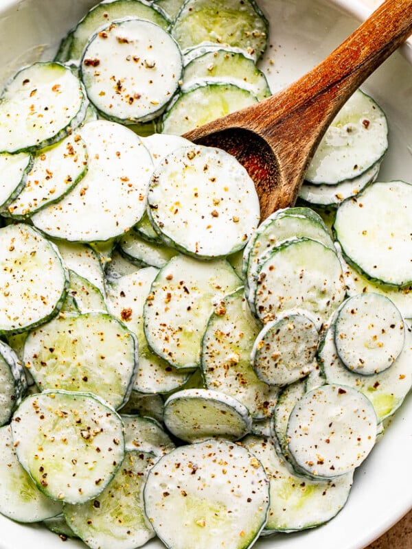 salad bowl filled with sour cream covered cucumbers sprinkled with cracked black pepper