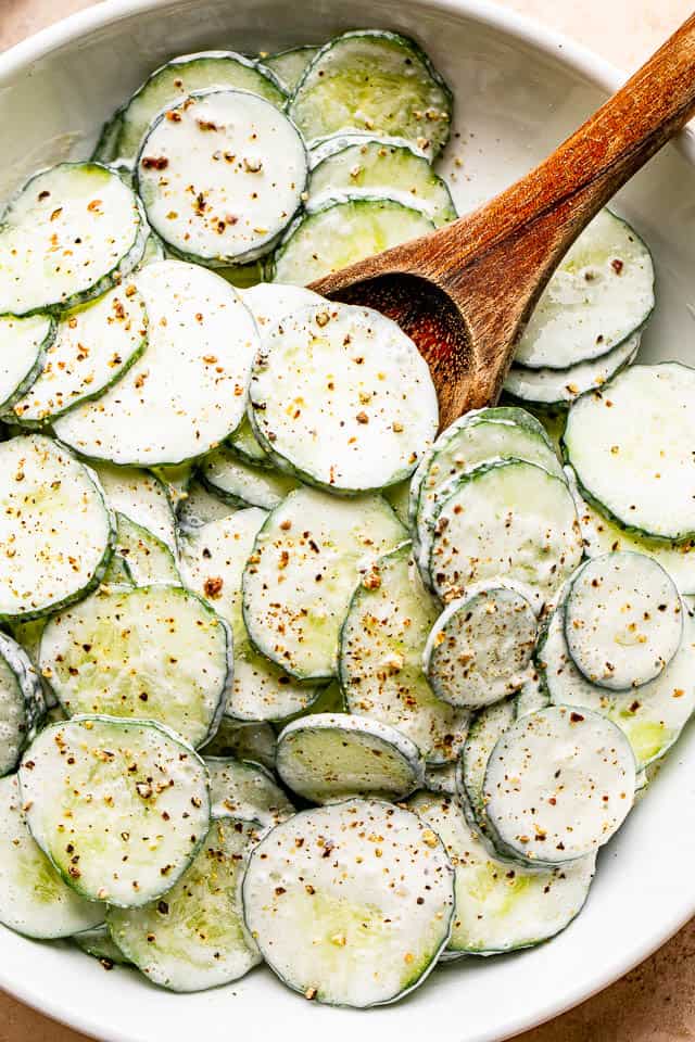 salad bowl filled with sour cream covered cucumbers sprinkled with cracked black pepper on top.