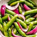 roasted sugar snap peas with red onions served in a cream bowl