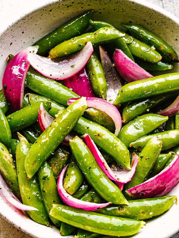 roasted sugar snap peas with red onions served in a cream bowl