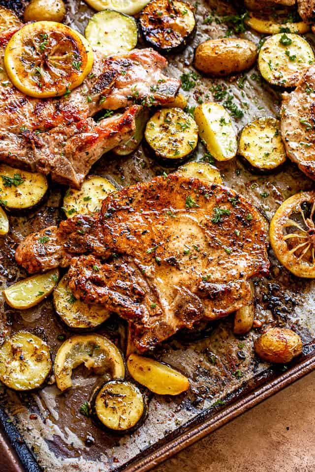 sheet pan with baked pork chops on top of slices of squash and lemons