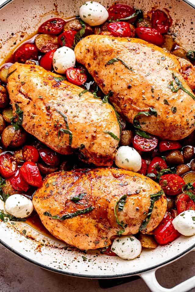 chicken breasts brushed with balsamic vinegar and set next to cherry tomatoes, mozzarella cheese balls, and garnish of basil