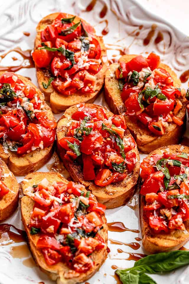 white platter with toasted bread sliced covered in tomato salad with balsamic glaze