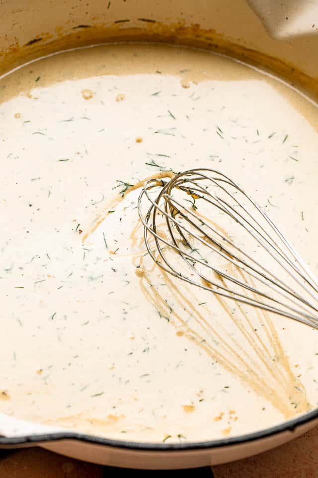 whisking a cream sauce inside a white pan